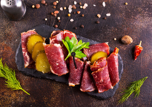 Dried Pastrami slices, beef meat with herbs on black board.