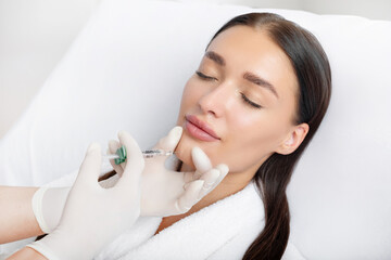Cosmetologist makes lipolytic injections to correct chin of young woman. Female aesthetic...