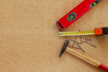 Hammer, tape measure, red spirit level and nails on cork.