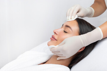 Beautician cleaning skin by using cotton pads or sponges, relaxed woman getting facial care at spa salon, free space