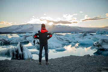 A man in a winter jacket and hat, standing against a backdrop of glaciers and a lake.