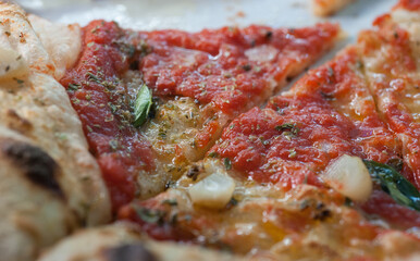 Close-up of sliced Neapolitan Margherita pizza with tomato sauce, basil, mozzarella, olive oil, garlic