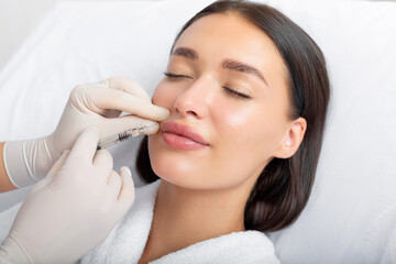 Beauty specialist making injection in female patient lips, lip augmentation and correction...