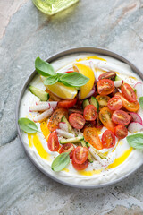 Plate of tirokafteri or greek feta dip sauce with fresh vegetables, vertical shot on a grey granite background, elevated view