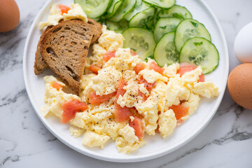 Scrambled eggs with smoked salmon and fresh cucumber salad served on a white plate, horizontal shot, middle close-up