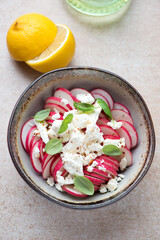 Bowl of radish and feta cheese salad, vertical shot on a beige stone background, high angle view