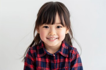 A smiling young girl with pigtails and a plaid jacket stands against a plain background. Her bright eyes and happy expression convey a sense of joy and charm.