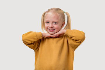 Portrait of a cute little girl with blond hair in a yellow sweatshirt, looking at the camera and smiling.
