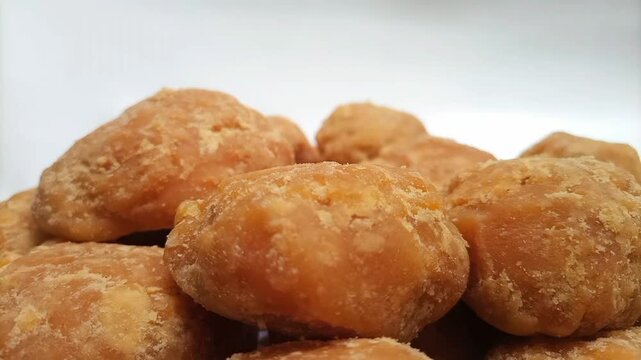 Micro shot of Jaggery or Gur pieces rotating on white background. Organic brown cane sugar pieces