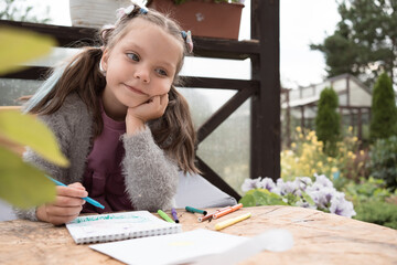 6 year old girl drawing and dreaming outdoors in garden