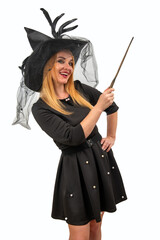Smiling young woman wearing a witch costume is holding a magic wand and posing on a white background