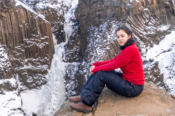 A woman sits on a rock in the snow, wearing a red sweater and black pants