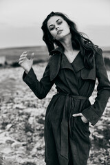 Mysterious woman in trench coat stands on rocky terrain with hands in pockets © VICHIZH