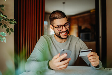 Young caucasian man shopping online on mobile phone using credit card

