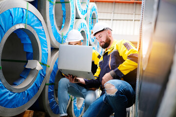 Male engineer works and inspects machinery at a metal sheet factory.