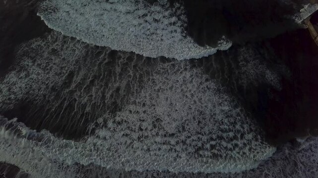 Aerial view of turbulent ocean waves crashing against the dark shoreline, Eyemouth, United Kingdom.