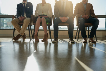 Waiting, interview and legs of business people in office for onboarding performance review with hr. Recruitment process, row and closeup of hiring candidates in a line for meeting in workplace lobby.