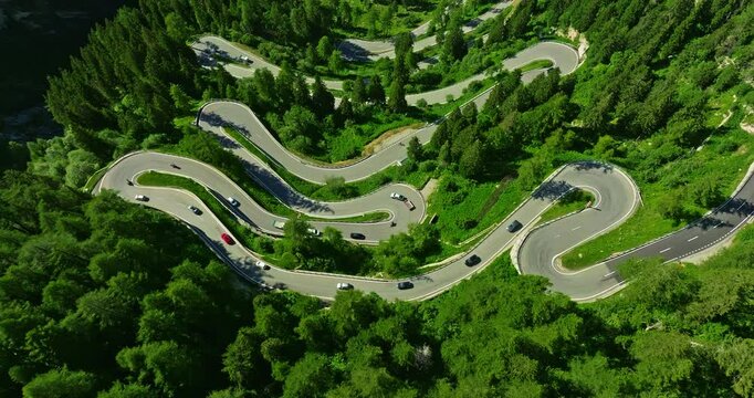 Aerial flyover over the turns of Maloja pass in Swiss. Aerial view of cars on road trip across the mountains of Switzerland drive along hairpin turns. Aerial drone view winding mountain road