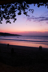 Fototapeta premium Mesmerizing Beach Sunset with Soft Purple and Pink Hues Reflecting on the Ocean Waters. The Scene Captures the Beauty of the Twilight Hours with Gentle Waves, Silhouetted Figures Strolling Along 