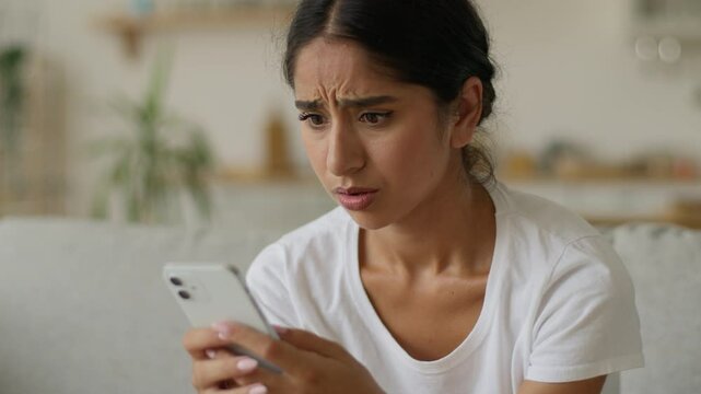 Portrait Muslim Islamic Indian woman Arabian girl female lady reading bad news reject refuse online lost lose at home looking at smartphone mobile phone internet problem trouble upset sad frustrated