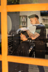 Fototapeta premium tattooed barber cutting the hair and beard of a young, dark-haired client.