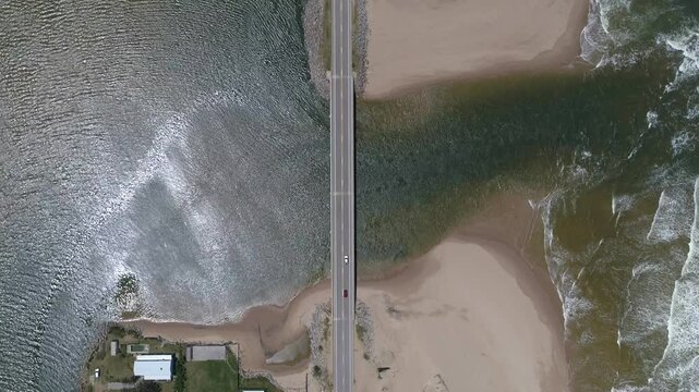 Aerial view of a beautiful beach with a serene bridge over the ocean and a car on the road, Jose Ignacio, Maldonado, Uruguay.