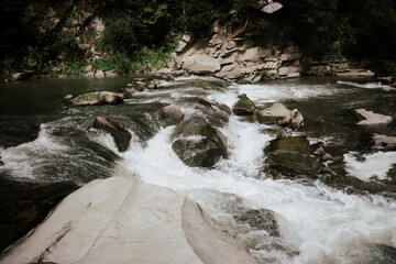 Fototapeta premium A serene river flowing over rocks in a lush green landscape with scattered boulders on a sunny day