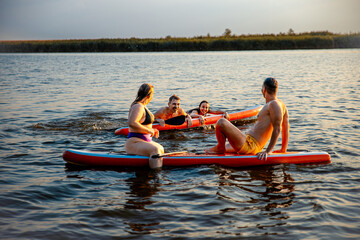 Group of friends on sup board enjoying a day at lake during sunset.