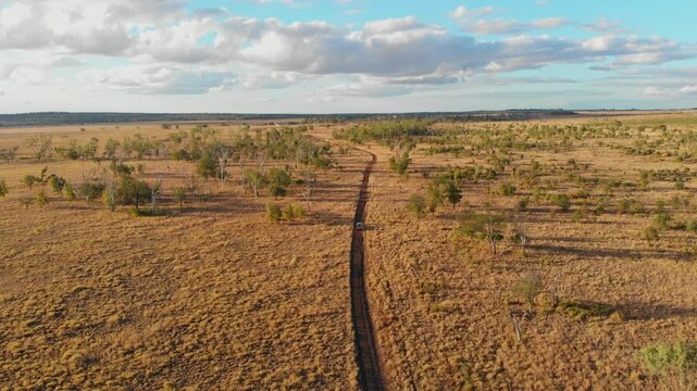 Aerial view of a vast and scenic outback landscape with a dirt road winding through dry bush and open space, Emerald, Queensland, Australia.