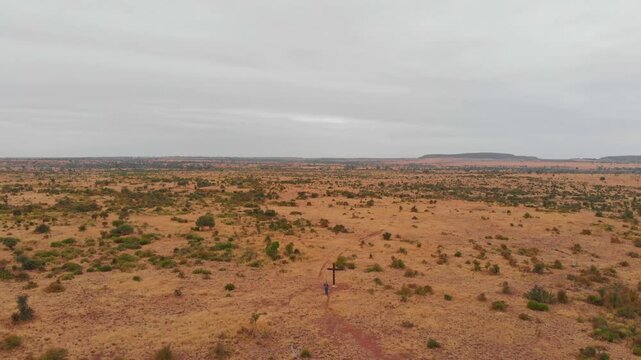 Aerial view of vast and barren outback landscape with a man and cross amidst bush, Mackenzie River, Queensland, Australia.