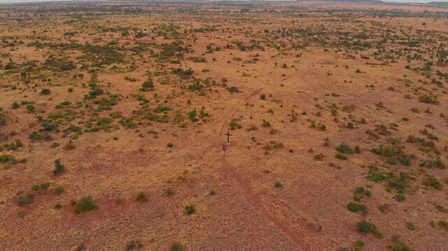 Aerial view of the rugged outback with a cross and a solitary man amidst the barren bushland, Mackenzie River, Queensland, Australia.