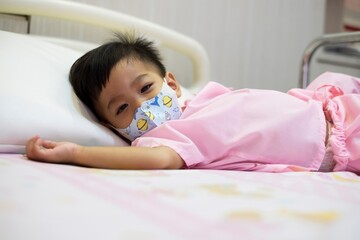 A young child lying on a hospital bed with a breathing tube in their nose.