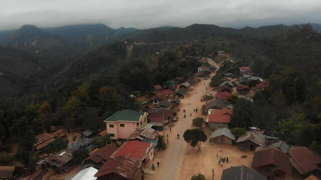 Aerial view of a picturesque village with traditional houses along a dusty road, surrounded by scenic mountains, Sam Neua, Laos.