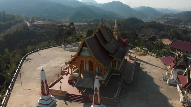 Aerial view of a beautiful temple surrounded by serene mountains and a traditional village, Sam Neua, Laos.