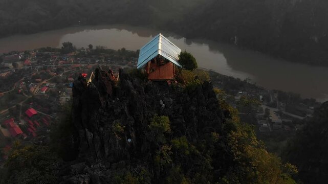 Aerial view of a picturesque village with wooden houses by a serene river and majestic mountains, Nong Khiaw, Laos.