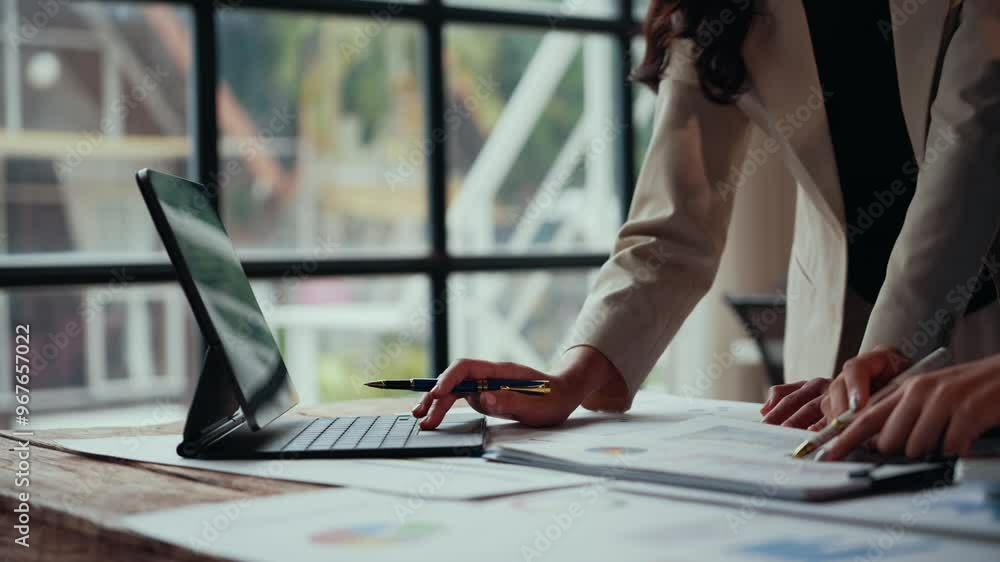 Poster businesswomen analyzing data on a convertible laptop, discussing insights, and pointing at charts an