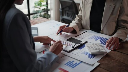 Businesswomen collaborating in an office setting, analyzing financial graphs and using a calculator to assess business profits and strategies for growth and success
