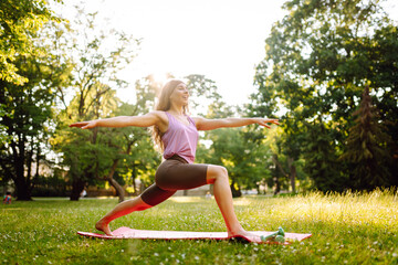 A woman practices yoga in a sunlit park while using a mat and weights on a warm afternoon. ....