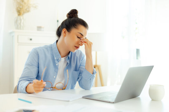 Photo of a tired arabian or indian business woman, company manager or digital seo, sits at a workplace, feels stressed and overworked, having migraine, headache, closes eyes and massaging bridgenose
