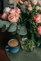 A bouquet of pink and white roses on a wooden table in the living room. A bouquet and a cup of coffee for the woman you love