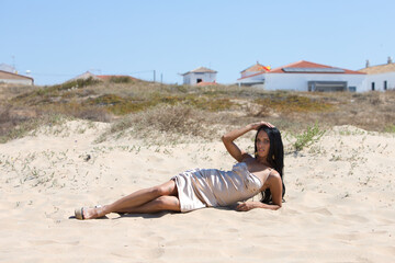 beautiful young brunette woman with long hair lying on a fine golden sand dune on a beach in the south of Spain in andalusia. The woman is wearing make-up, a long golden dress and high heels.