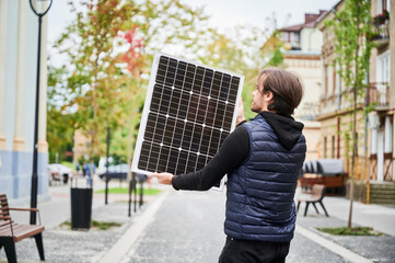 Man holding photovoltaic solar panel in front of historical building. Concept of integration of...