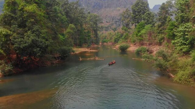 Aerial view of kids playing by a serene river with kano and buffaloes surrounded by lush trees, Kong Lor Cave, Laos.