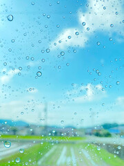 雨粒のついた窓ガラス越しに見る青空と日本の田舎の風景