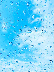 雨の水滴がついている窓ガラス越しに見える青空