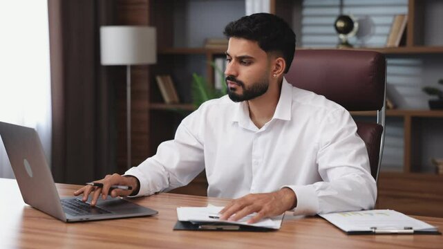 Side view of serious hindu businessman tapping on wireless laptop during handworking day in office corporate. Earnest male using modern gadgets for quality job.