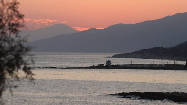 Gorgeous seascape with red sky, tiny chapel and large mountain slopes in the background on the remote greek island of Ikaria.