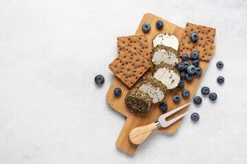 Soft goat cheese with blueberries and crispbread on wooden board on white background