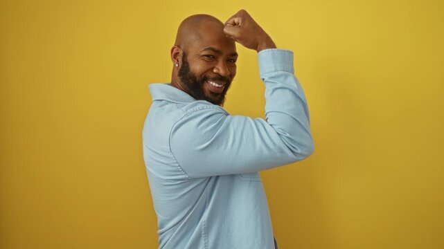 Young black man smiling and flexing muscles over isolated yellow background with confident expression