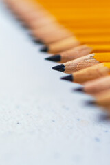 A diagonal row of penciils sit on a neutral table.  Focus on one pencil.  Copy space.